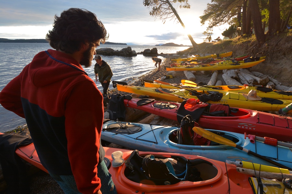 A man stands on the beach in front of a line of kayaks during an Outdoor Pursuits trip
