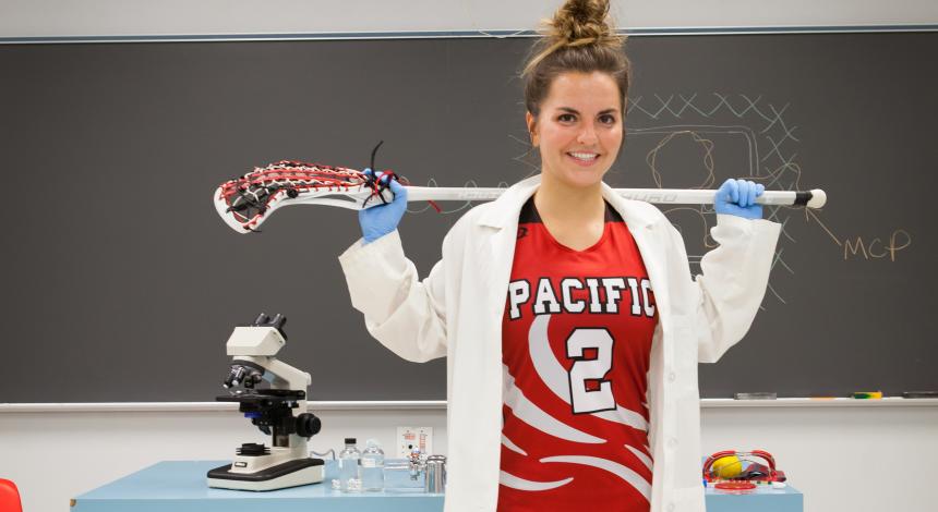 Mallory Hiefield poses in the biology lab with her lab coat and lacrosse gear