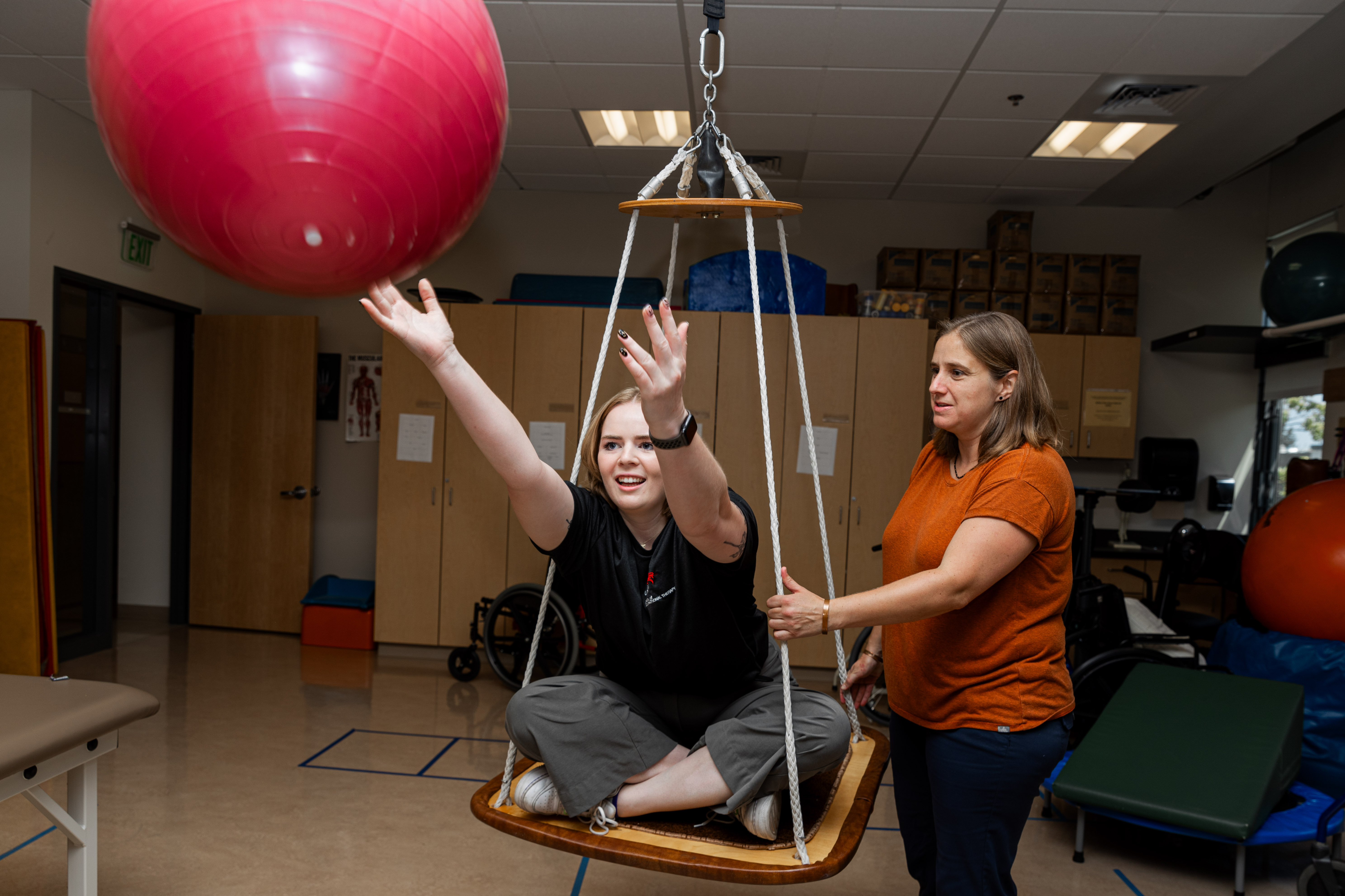 Two occupational therapy students demonstrate a therapy exercise that facilitates throwing and catching a yoga ball.