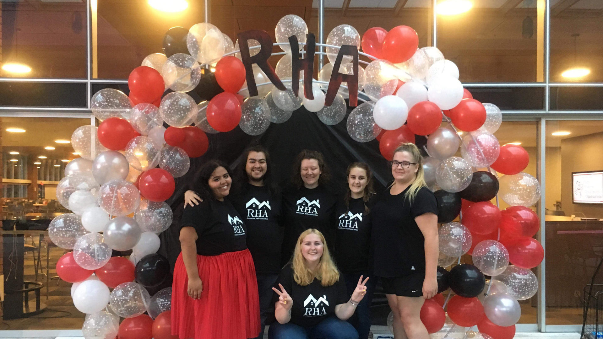 5 students in RHA shirts stand in front of a red and white balloon arch
