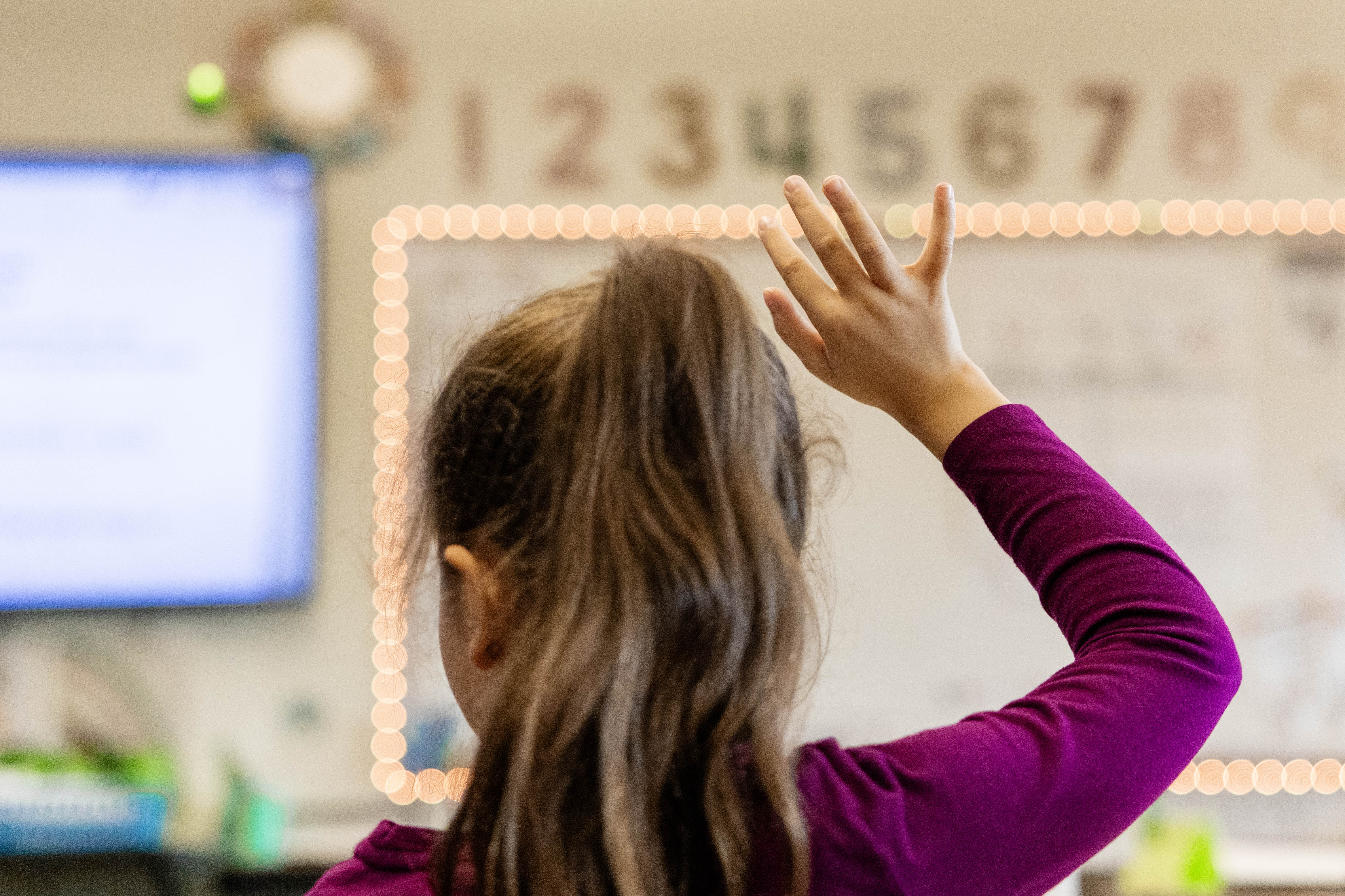 An elementary school student raises their hand in a classroom.