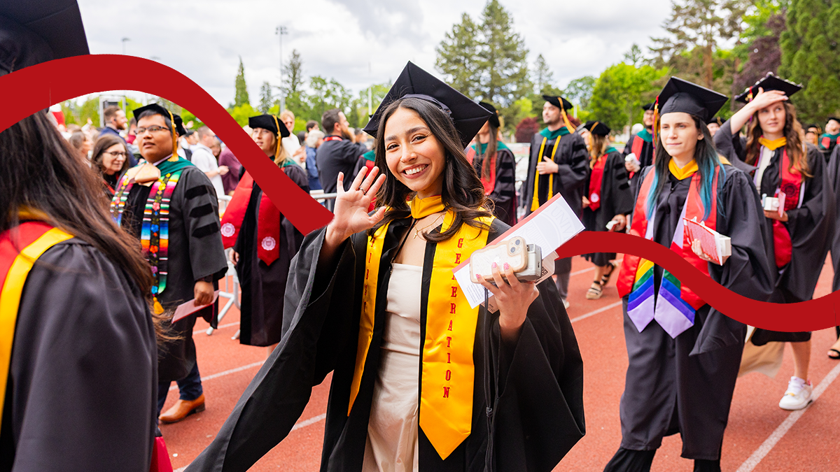 A Pacific student wearing a black graduation cap and gown and yellow "first generation" stole waves to the camera while processing with fellow graduates at commencement.