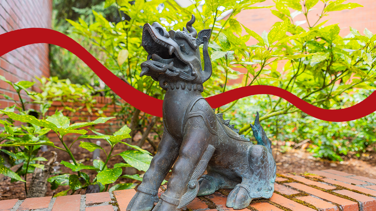 The twin statue of Boxer II sits on a brick wall with green plantlife behind it.