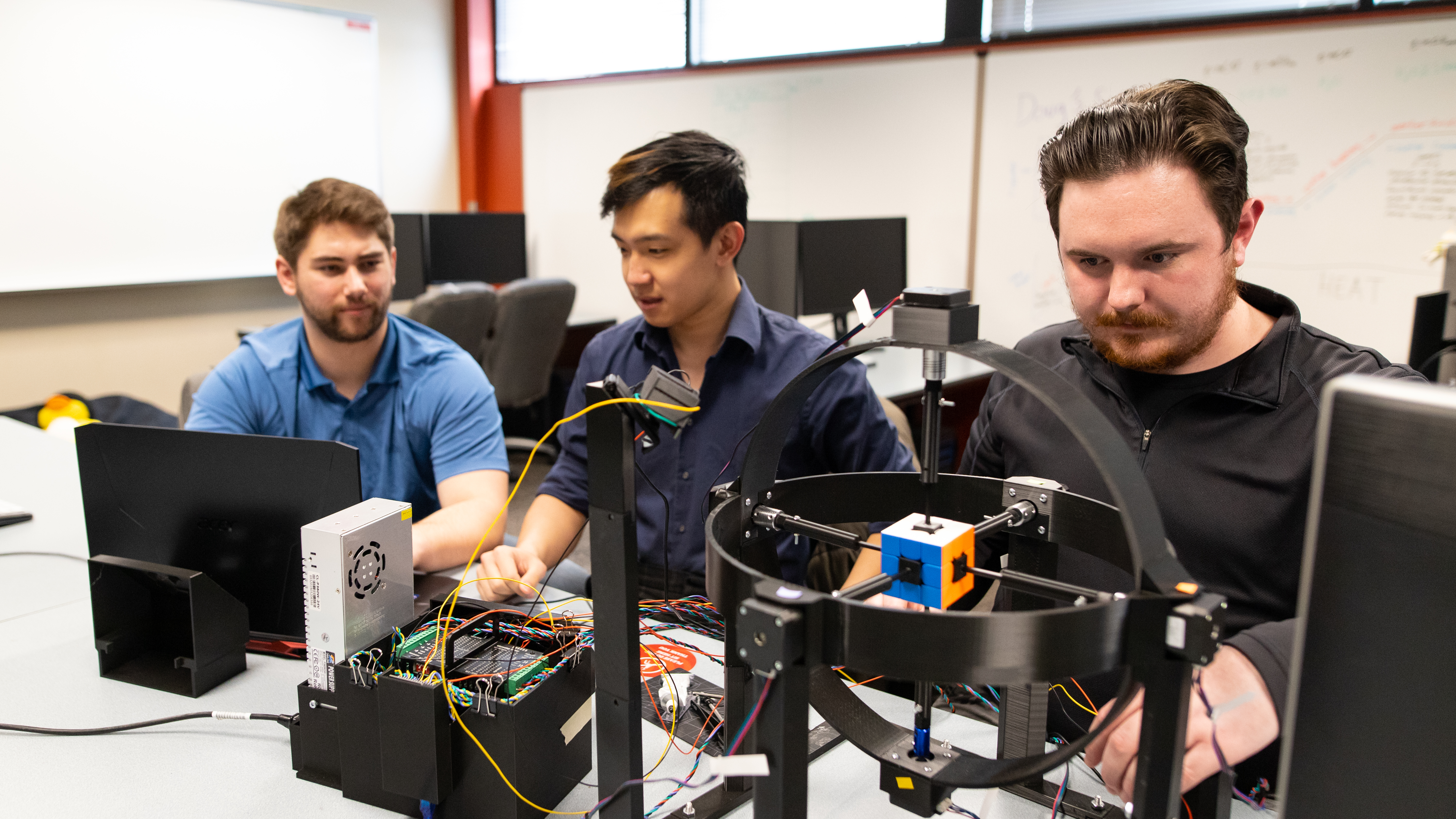 Three Pacific University Computer Science students working with computers and a rubiks cube