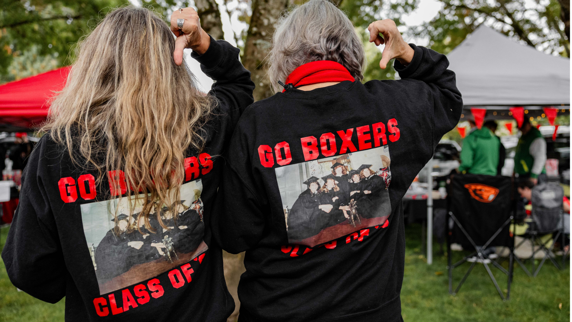 Two alumni show the back of their T-shirts that proclaim their class year