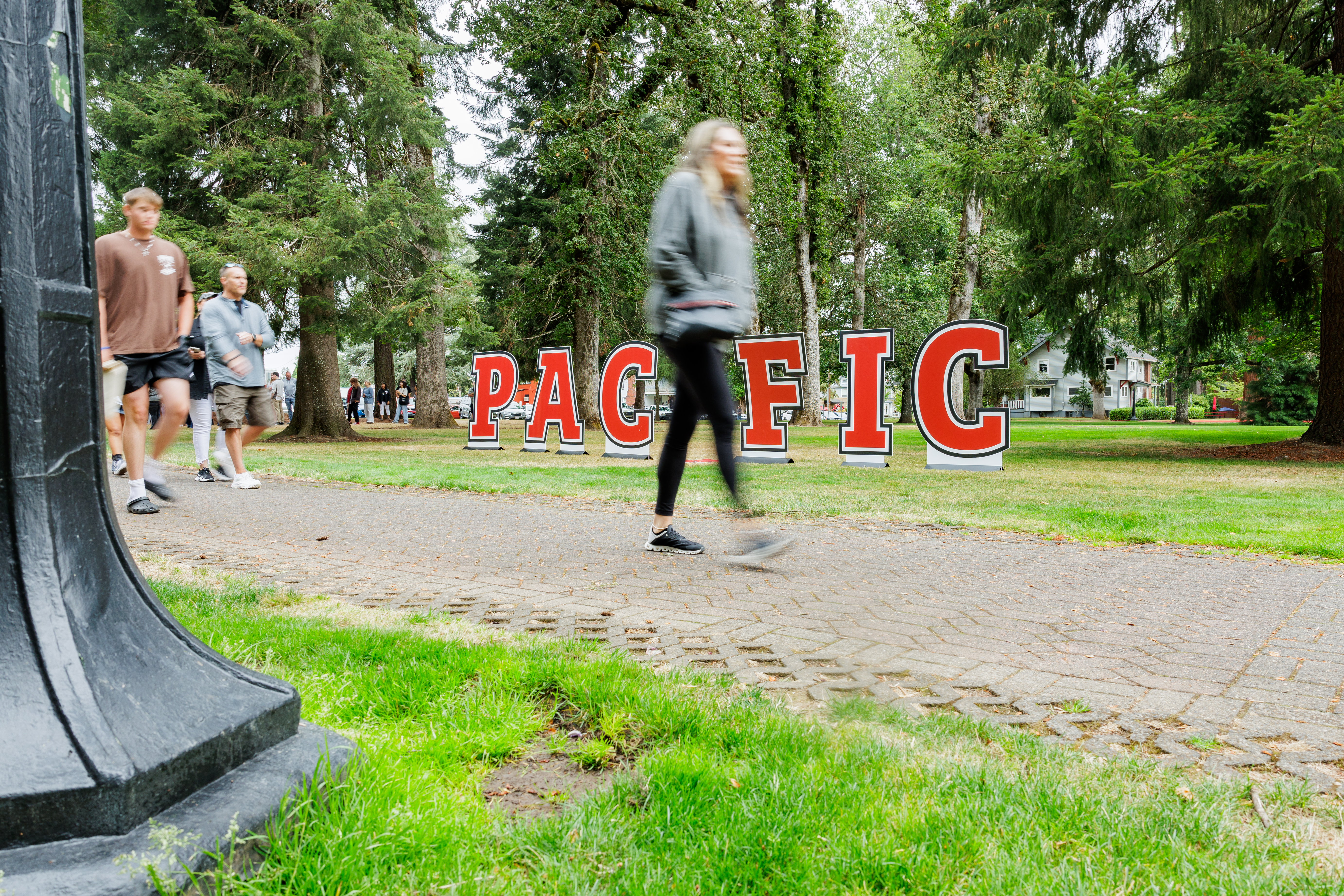 student walking in front of a Pacific University sign