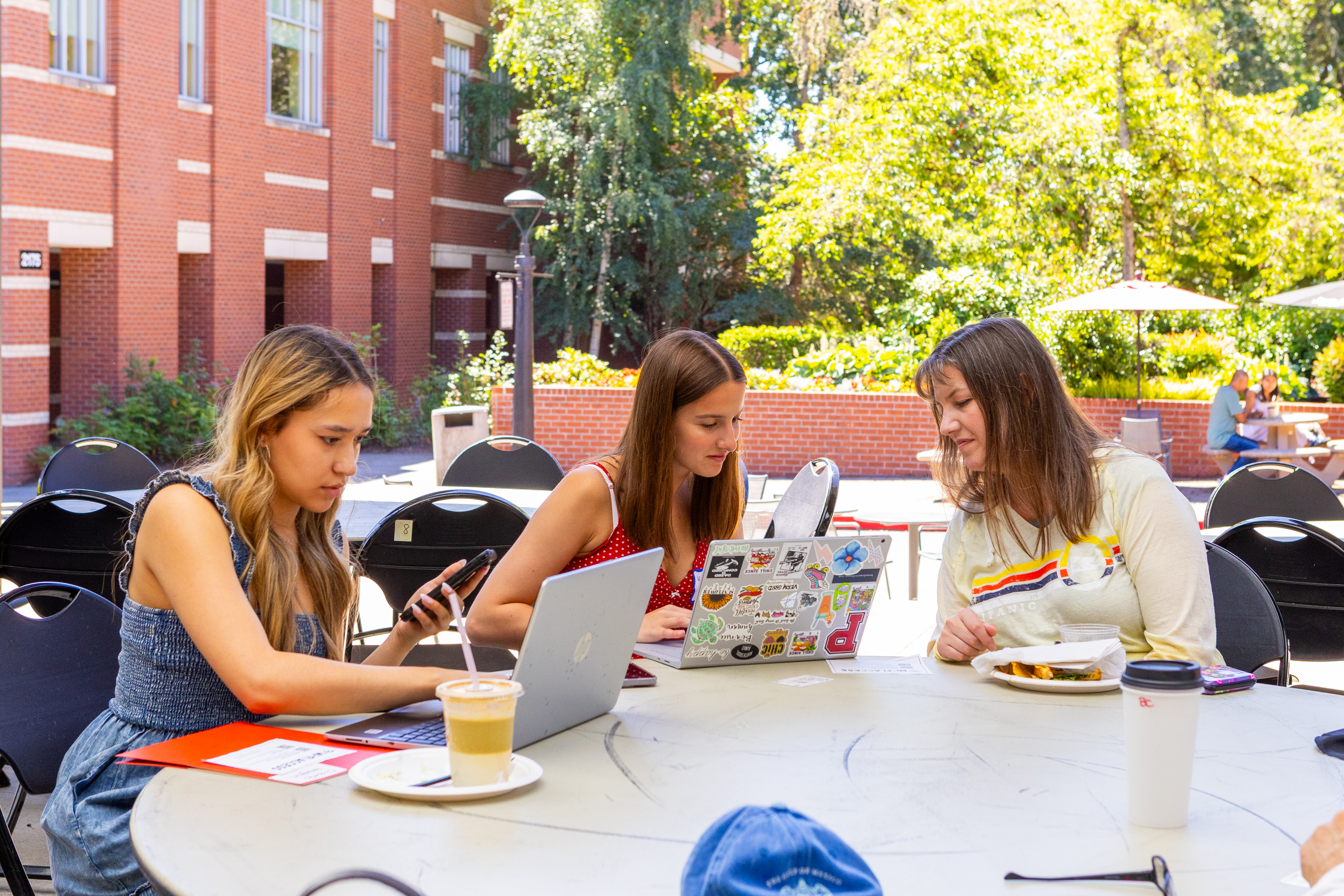 three Pacific University students sitting at a table on campus looking at laptops