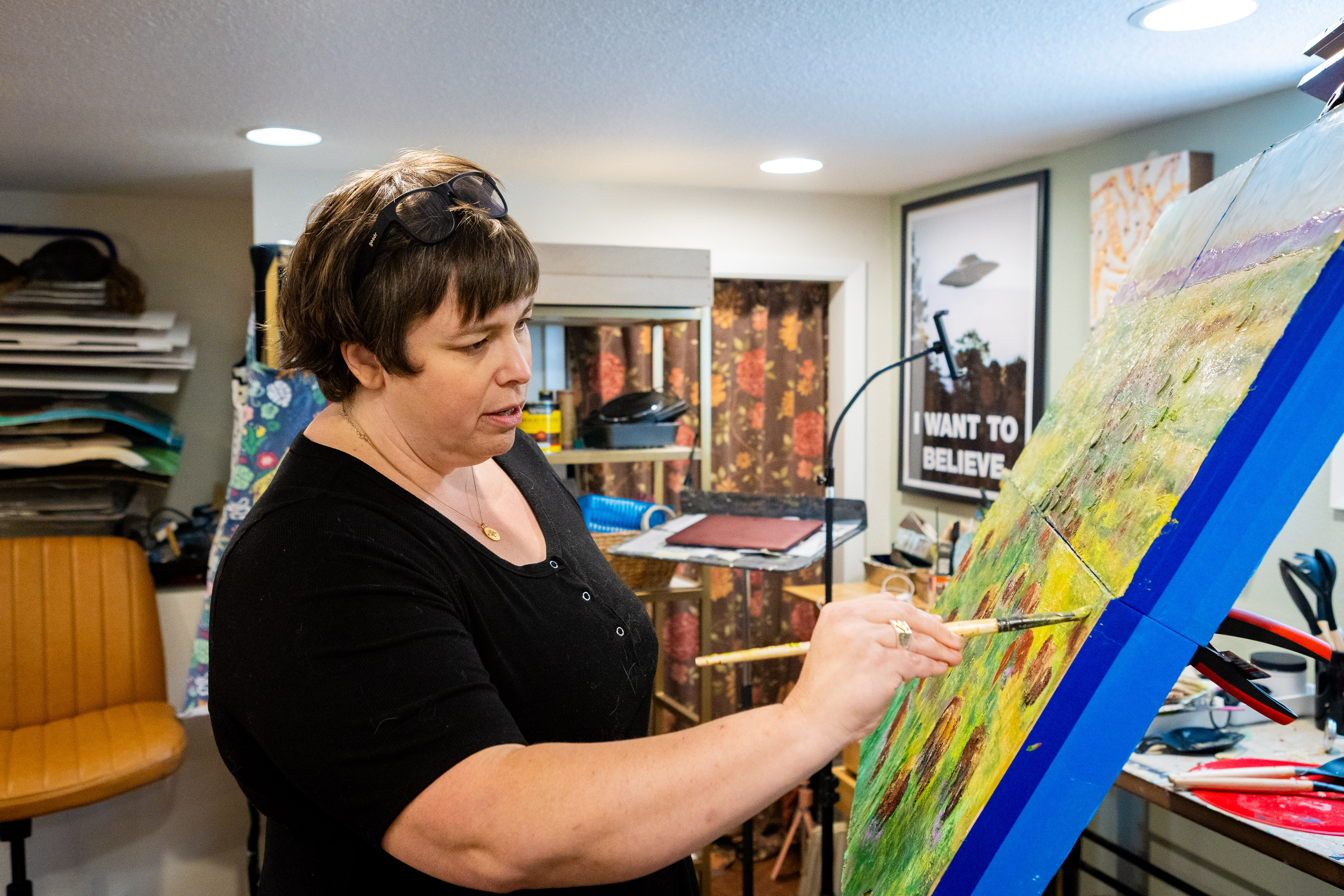Stevie Woods paints on a canvas in her home basement studio.