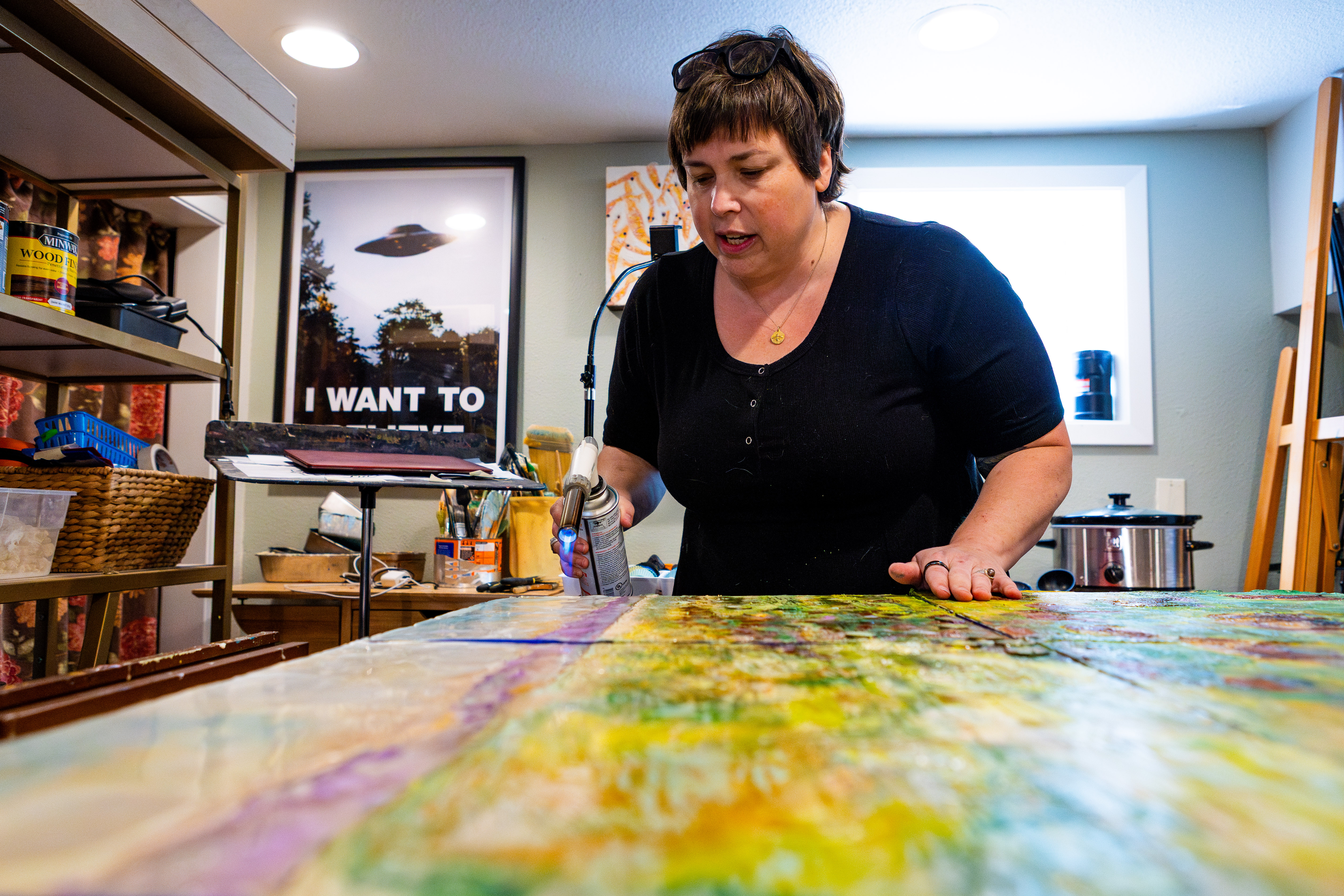 Stevie Woods holds a blowtorch over a canvas that is laid flat on an easel.
