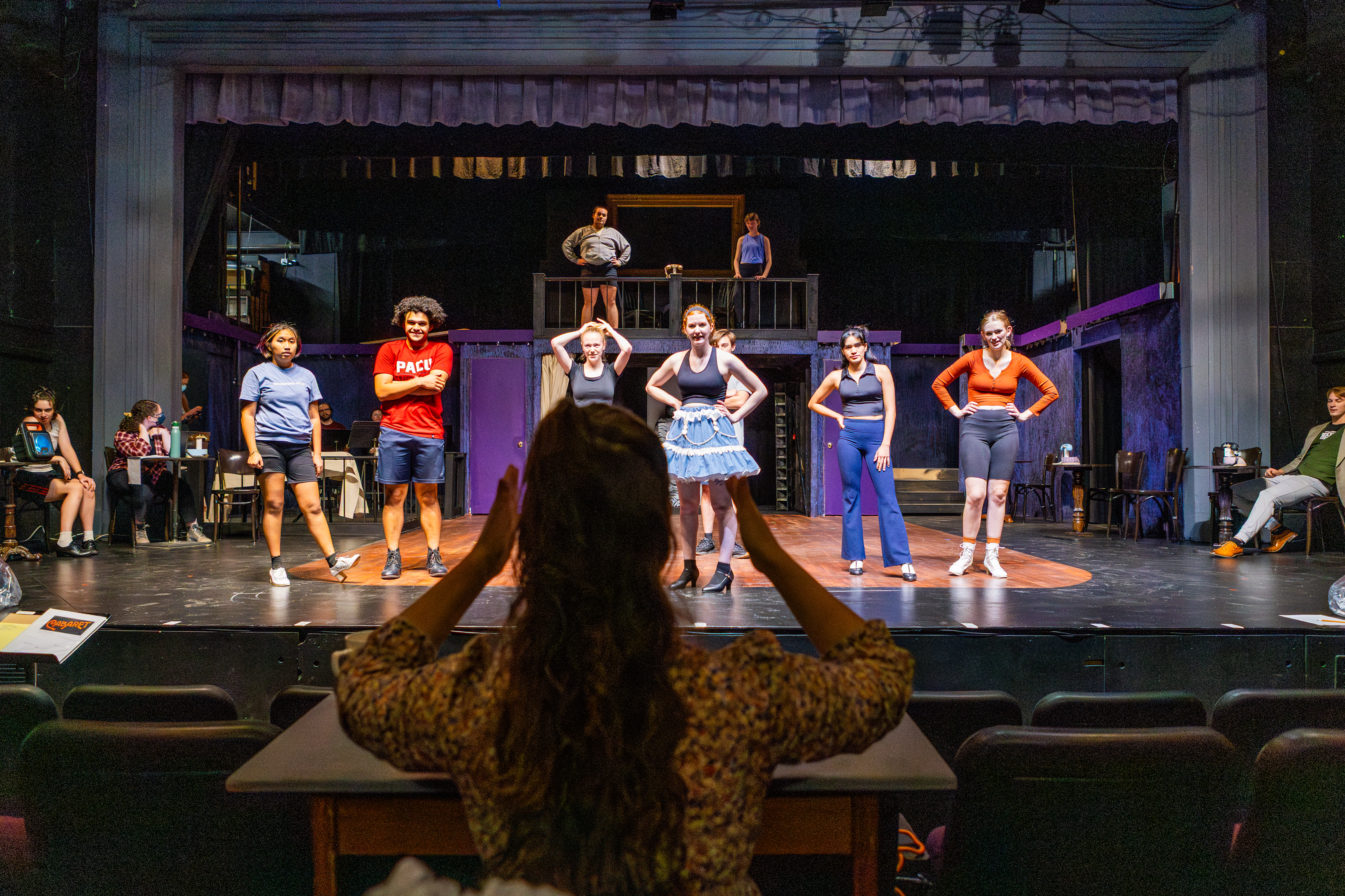 students rehearsing on a stages with director standing in front with arms raised