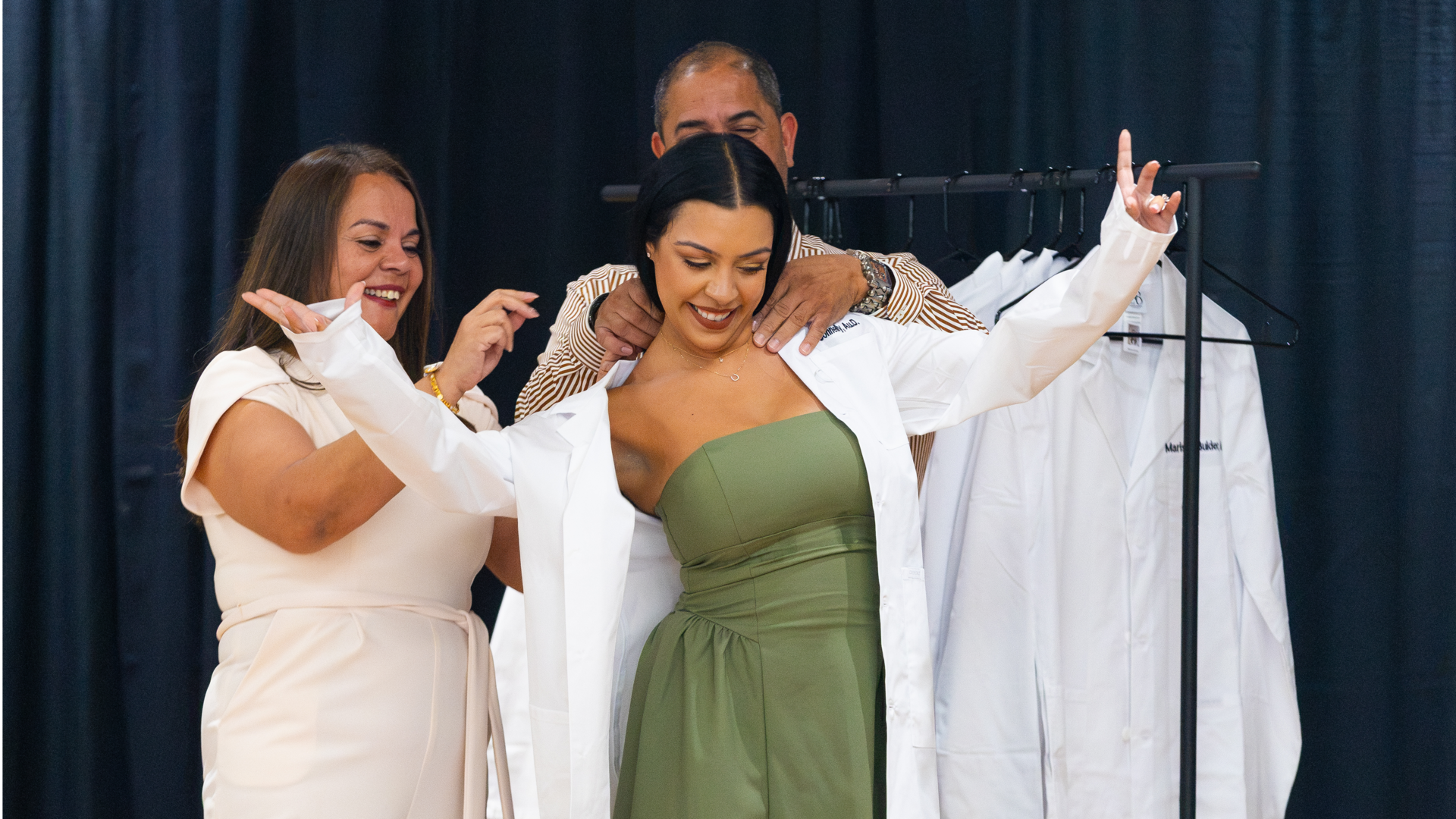 Family members help an audiology student don her white coat during a ceremony
