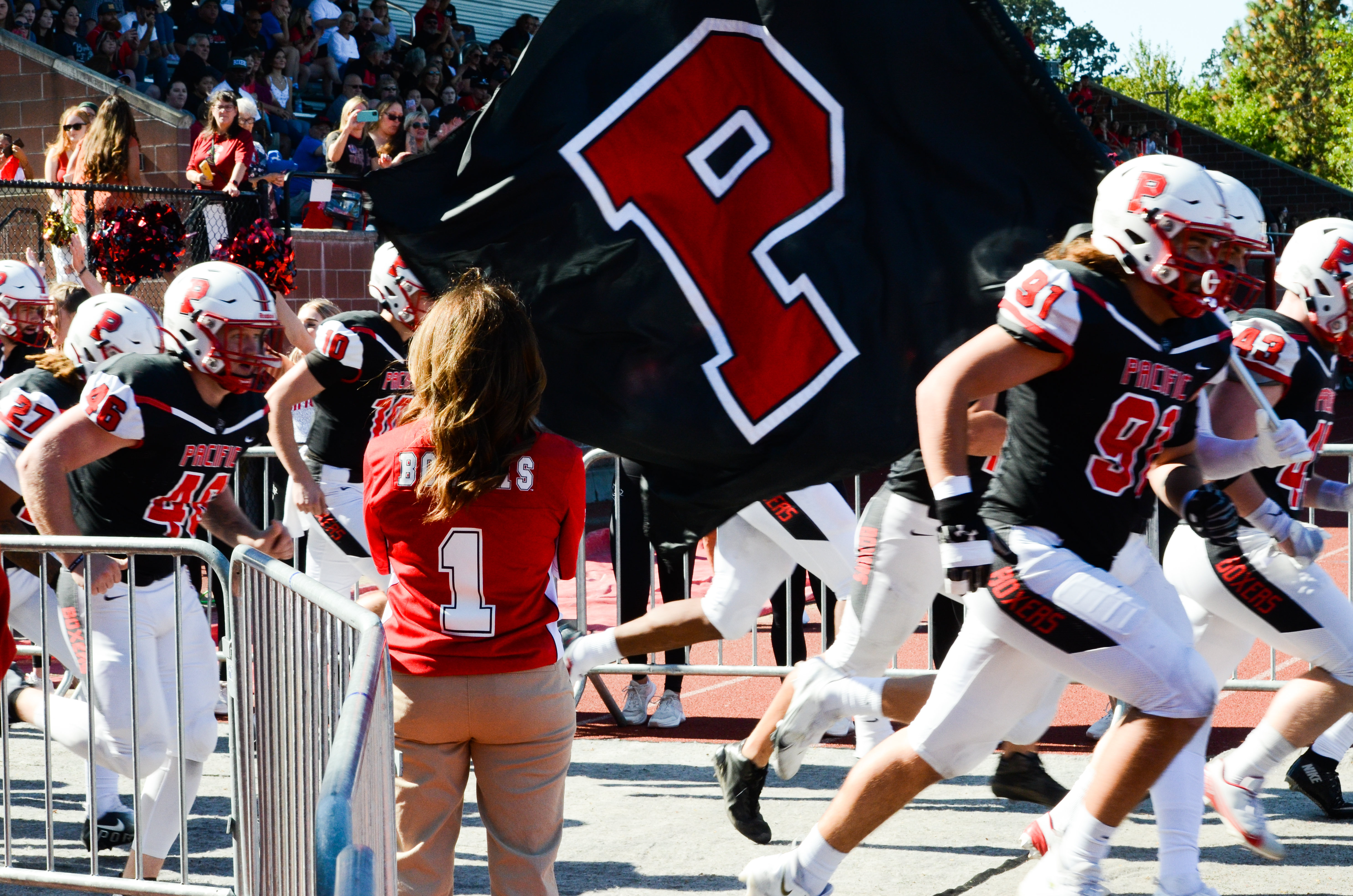 Members of the Pacific University football team run onto the field while carrying a Pacific University flag.
