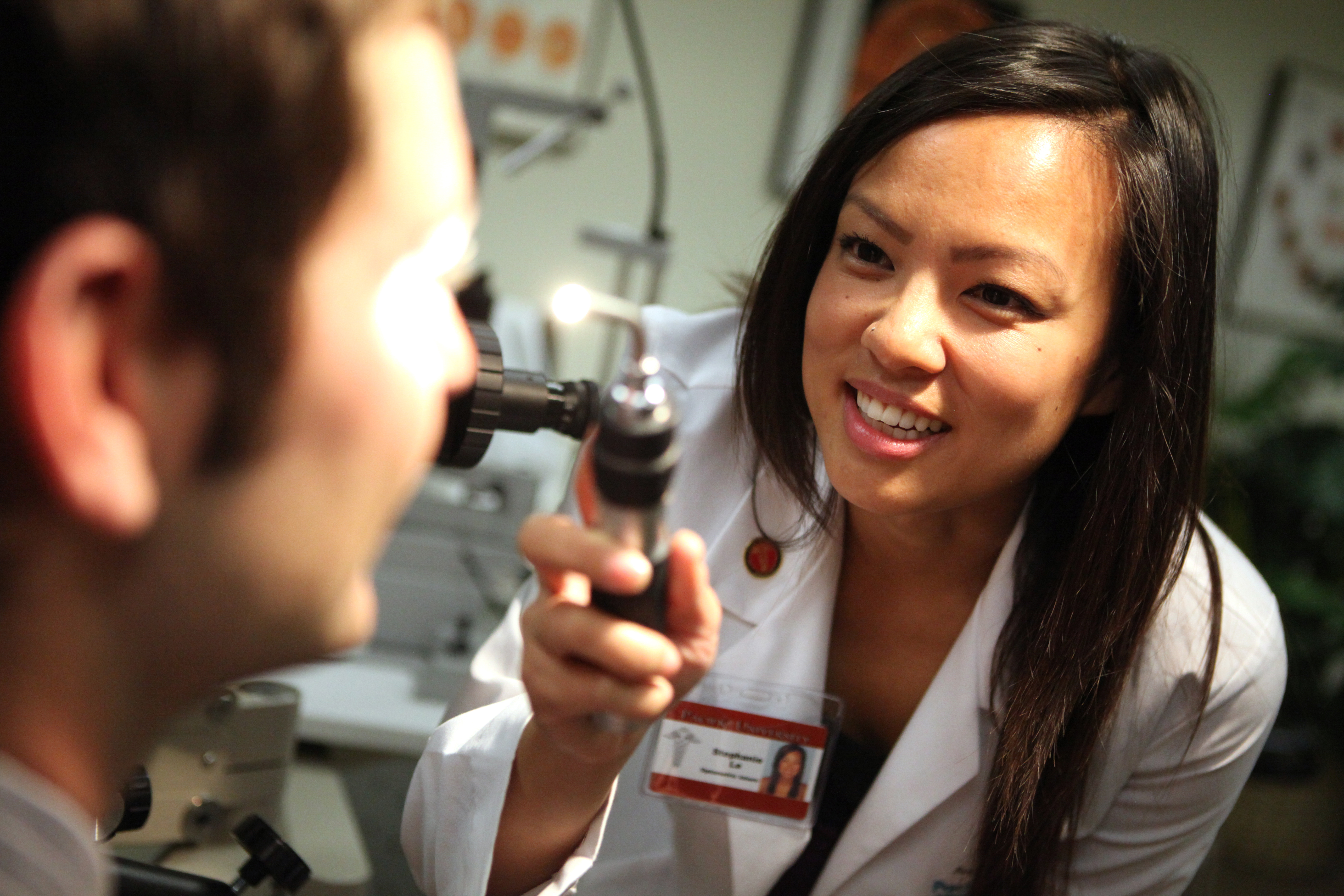 An optometry student examines a patient's eyes using a retinoscope.