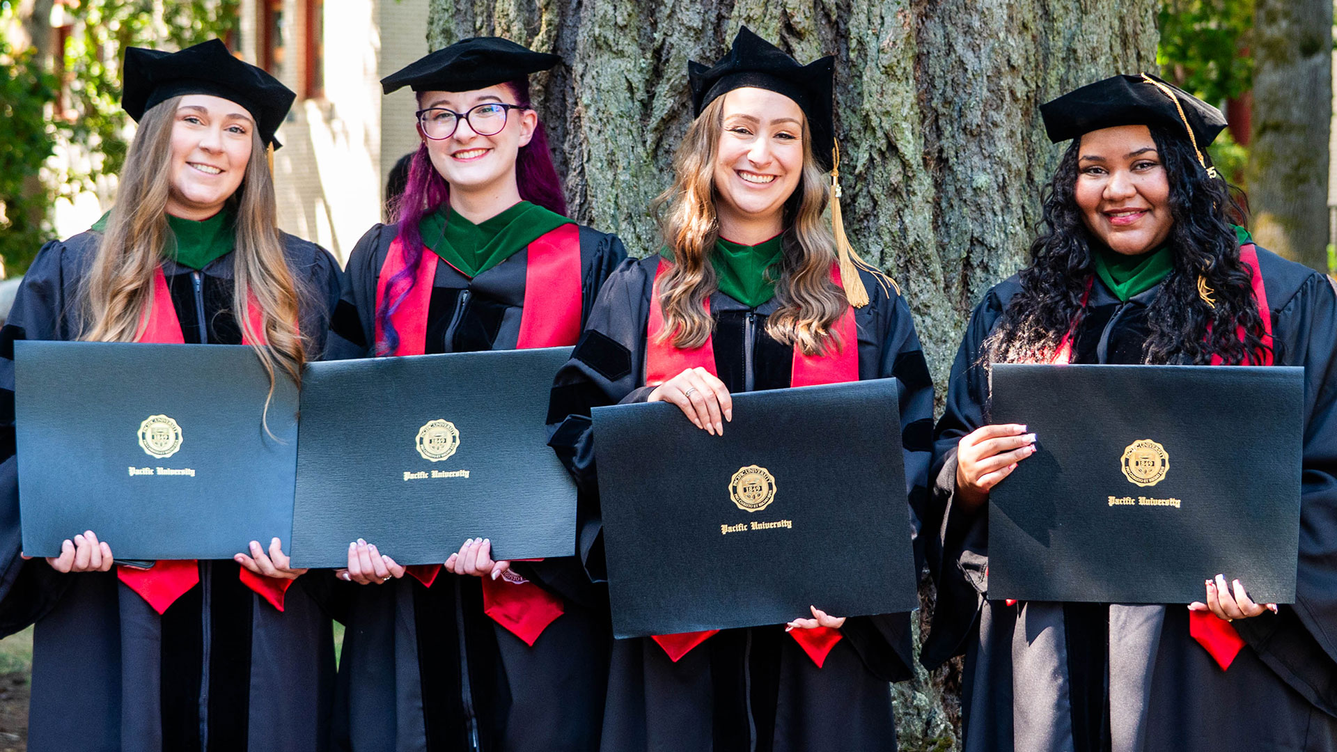 Four graduates holding their diplomas in front of them.