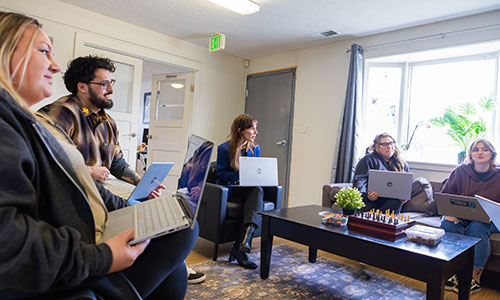 Five people holding laptop computers talk in a meeting.