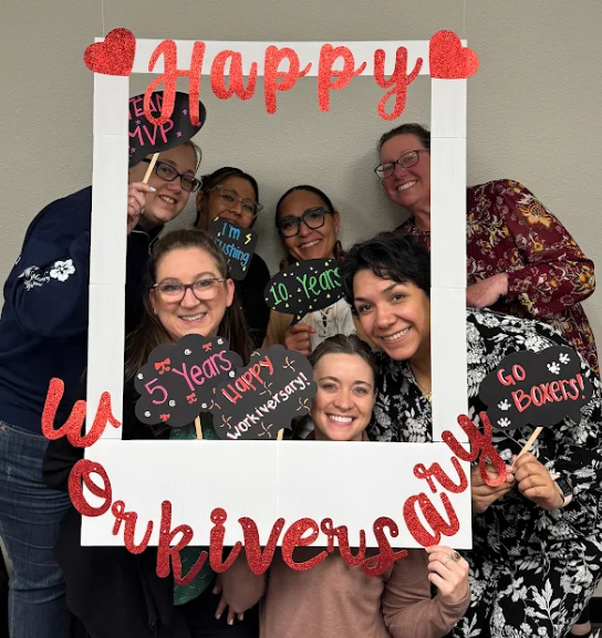 Human Resources team posing in a polaroid photo that says "Happy Workiversary" and holding fun signs to celebrate years of service. 