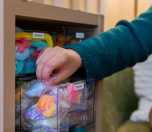 A hand reaches into a bin of squishable fidgets in Pacific's sensory room.