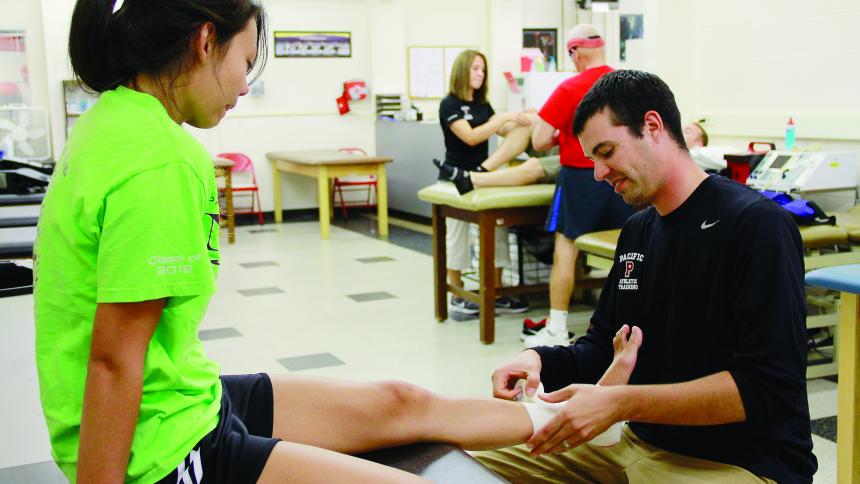 An athletic training student in a clinic wraps the ankle of a young female patient.