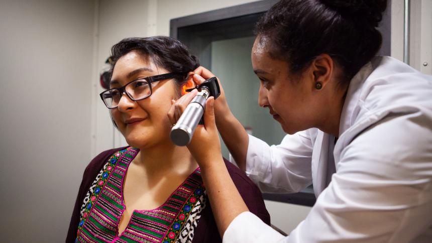 An audiology student uses an otoscope to examine a patient's ear canal. 