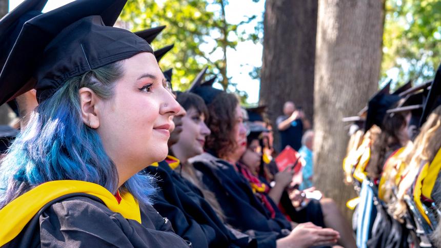Graduates sit under the oaks on the Forest Grove Campus during August Commencement 2023.