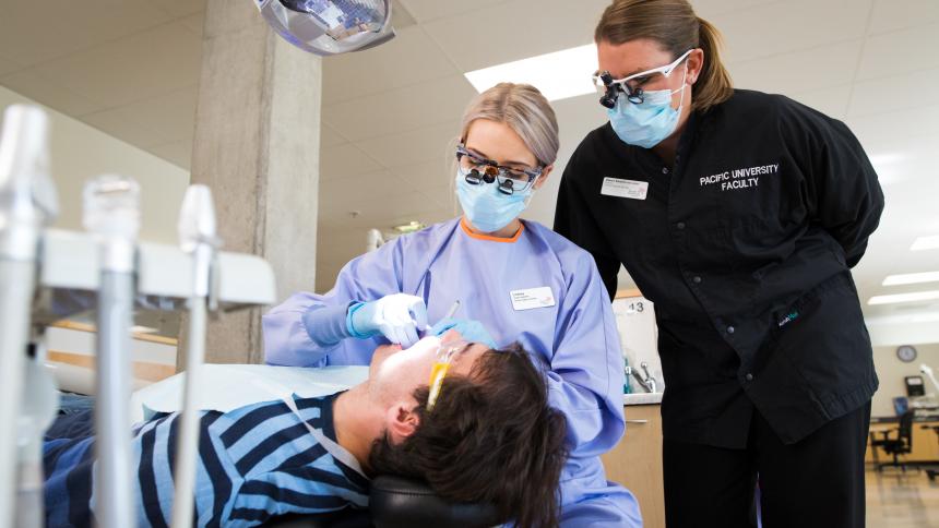 A dental hygiene students cleans a patient's teeth under the supervision of a faculty member.
