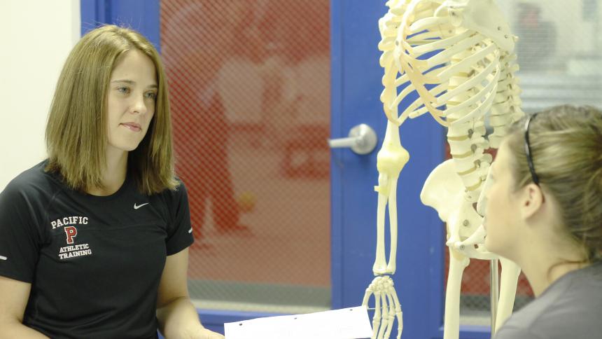 Kinesiology student in a kinesiology or physical therapy lab with a plastic skeleton