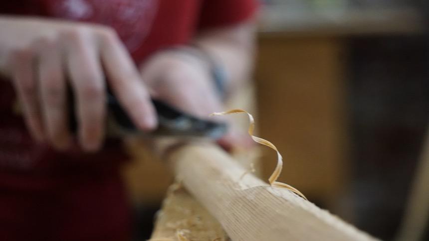 A student carves out a piece of wood building a Greenland paddle. 