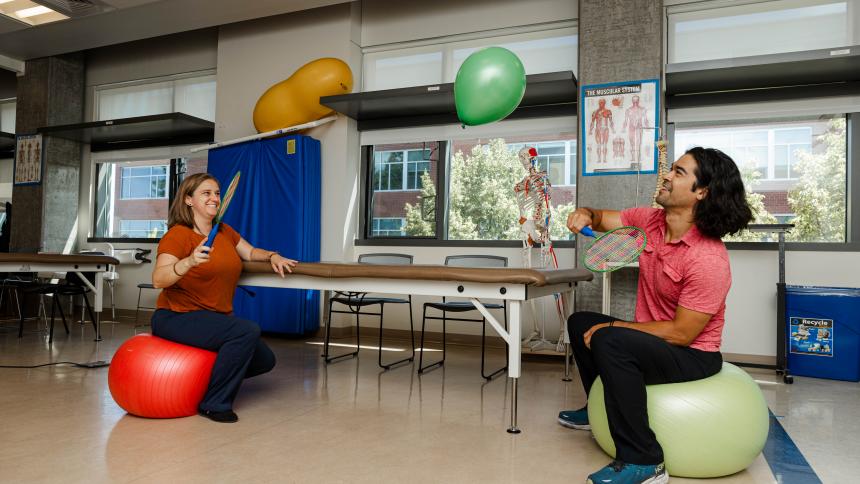 Two occupational therapy students demonstrate a common therapy exercise using balloons. 