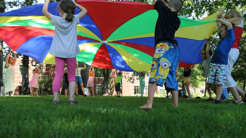 Children playing with parachute outside in sunshine.