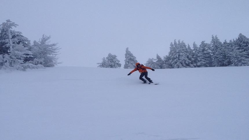 A snowboarder navigates down a snow-covered hill. 