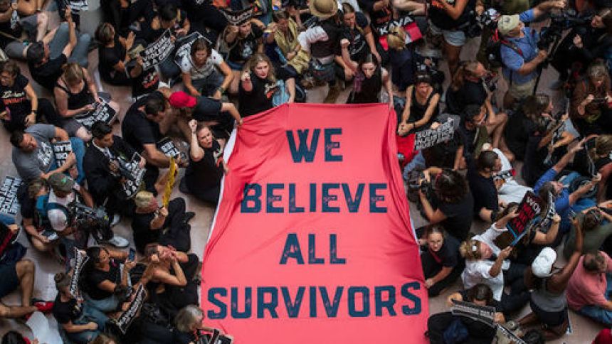 people holding a banner reading "we believe all survivors"