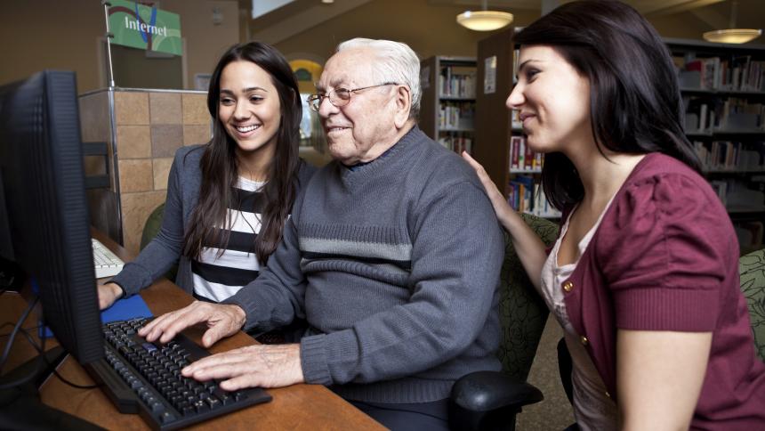 Two social work students help an elderly man use a computer.