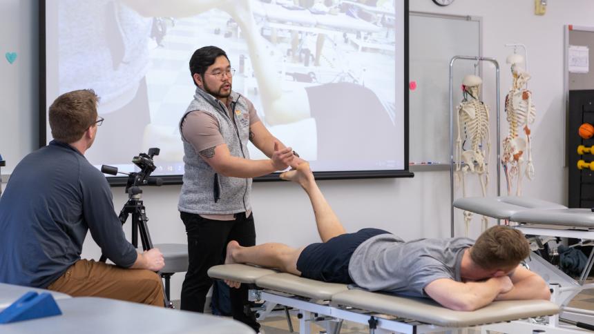 A physical therapy instructor demonstrates a way to strengthen the foot and leg on a student.