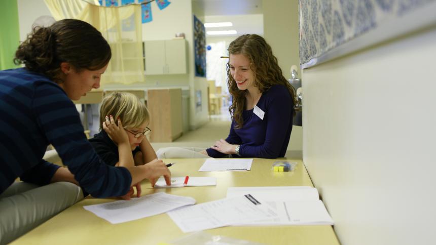 A speech therapy student works with a child and their adult in a speech pathology clinic.  