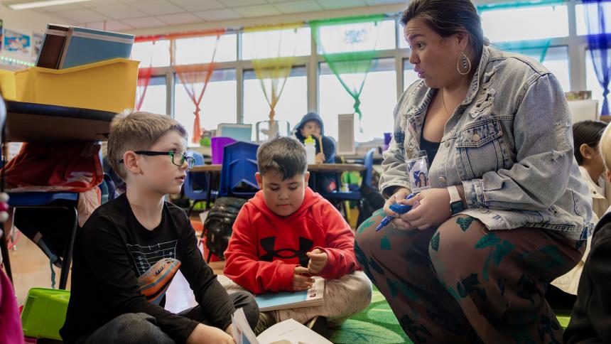 A student teacher help an elementary school student in a classroom setting.