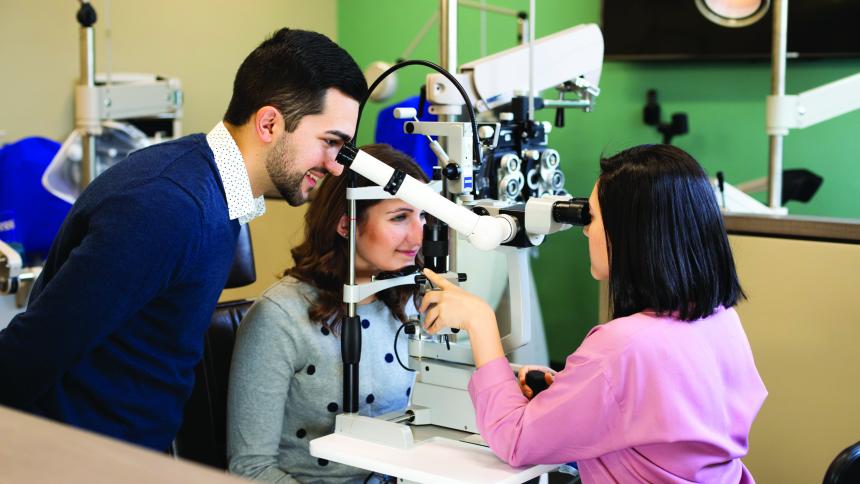 Two optometry students examine a patient's eyes during a routine exam.