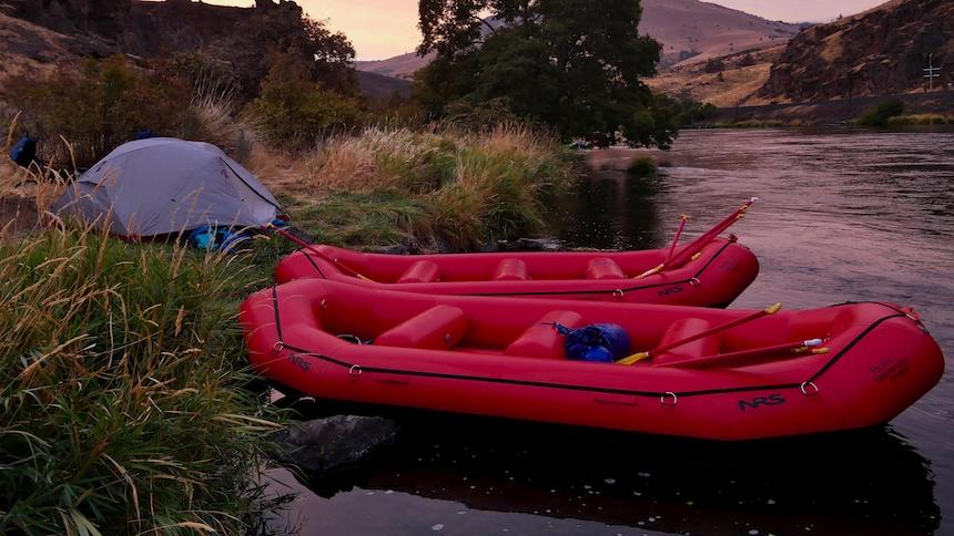 Two rafts rest on the bank near a tent at sunset on the river. 
