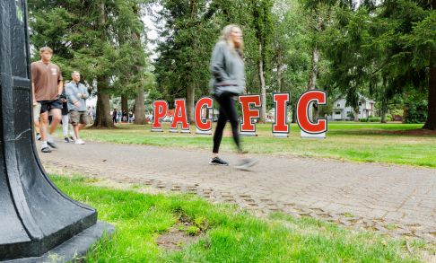 student walking in front of a Pacific University sign