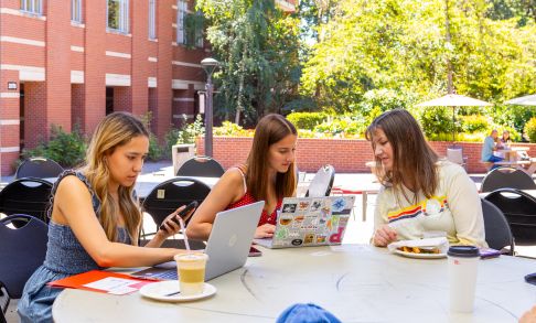 three Pacific University students sitting at a table on campus looking at laptops