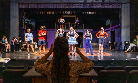 Students on stage rehearsing a play at Pacific University. Director stands in front with hands raised.