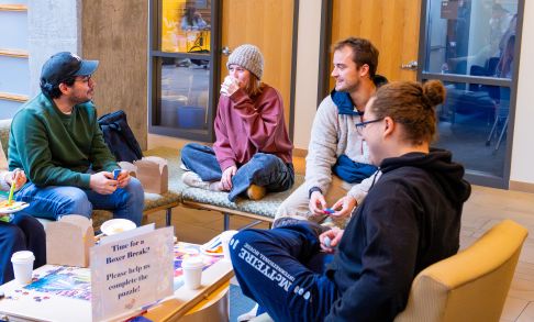 group of Pacific University Students sitting in chairs around a puzzle and  taking a break