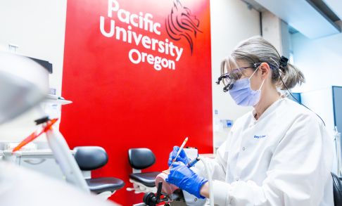 Amy Coplen, director of the school of dental hygiene studies, practices with a red Pacific University sign in background