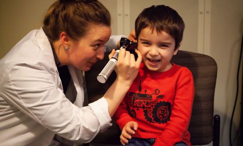 A Pacific audiology student uses an otoscope to look into a young child's ear.