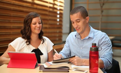 Two students sit at a table studying over an open textbook.