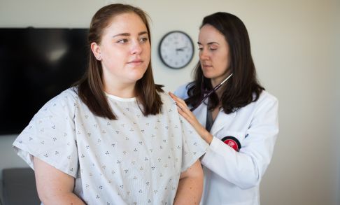 A physician assistant studies student listens to a patient's lungs using a stethoscope.