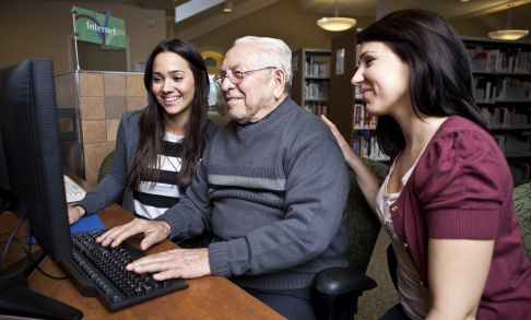 Two social work students help an elderly man use a computer.