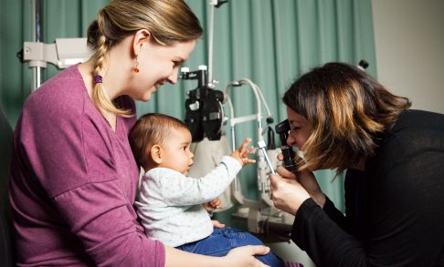 A mother has her baby's eyes checked by an optometrist.