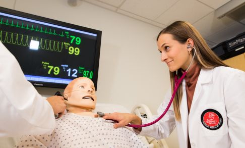 A physician assistant studies students practices using a stethoscope on a medical dummy.