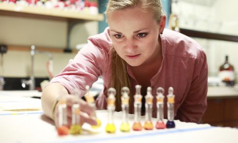 A female student aligns multicolored liquids in small glass jars by the darkness of their pigment.