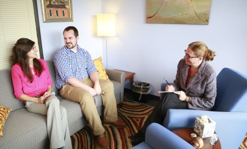 A clinical psychologist leads a therapy session for a young couple.